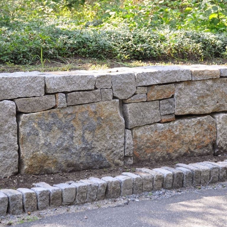 Close-up image for Reclaimed Granite Block Wallstone - Block Mix. The surface finishes shown are weathered and worn. The dominant color shown is gray; with brown and purple secondaries. Exhibits "movement" and the color mix creates a warm feeling. Speckled and blotched color patterns.