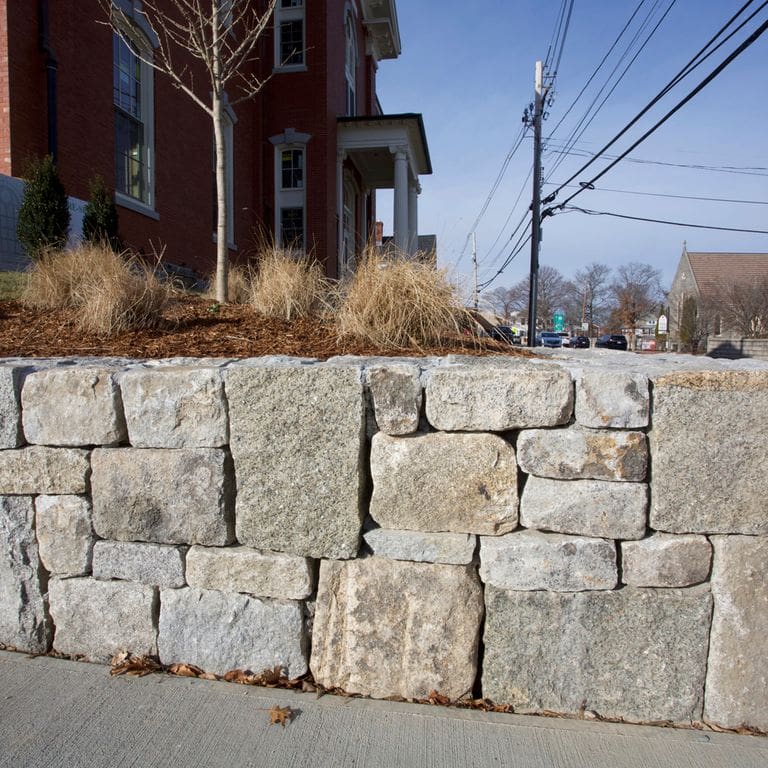 Application image for Reclaimed Granite Block - Wallstone. The image shows this product being used in a landscape wallstone application. The dominant color shown is gray.