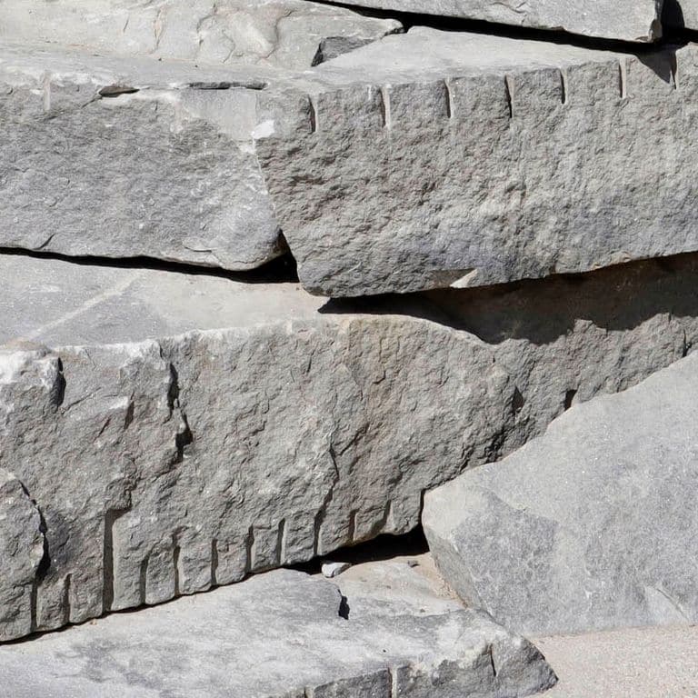 Close-up image for Reclaimed New England Granite Quarry Tailings - Oversized Wallstone. The surface finish shown is weathered. The dominant color shown is gray; with beige, purple and white secondaries. Exhibits "movement" and the color mix creates a cool feeling. Regular and cloudy color patterns.