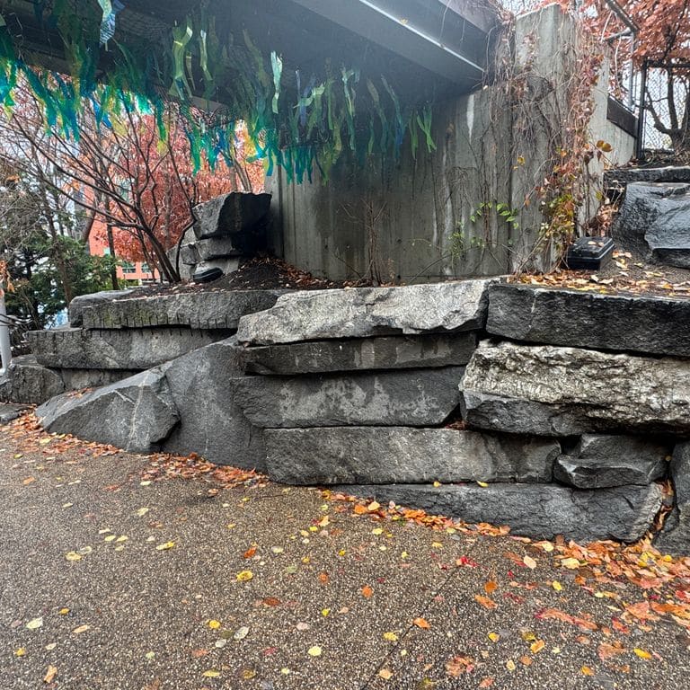 Application image for Granite - Reclaimed New England Quarry Tailings - Oversized Wallstone. The image shows this product being used for landscape wallstone and retaining wall. The dominant color shown is gray.