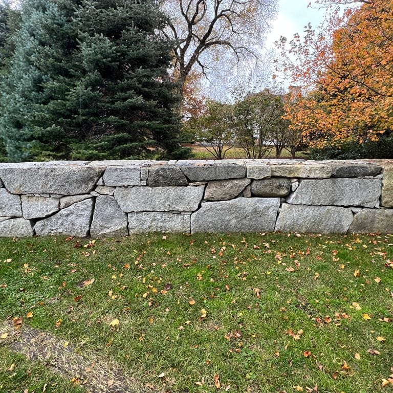 Application image for Granite - Reclaimed New England Quarry Tailings - Oversized Wallstone. The image shows this product being used in a landscape wallstone application. The dominant color shown is gray.