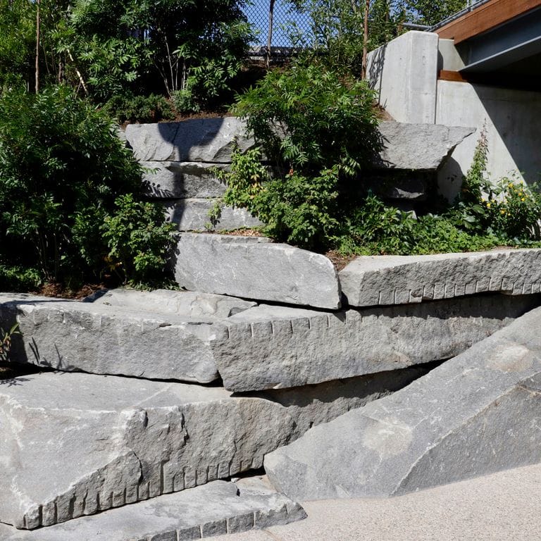 Application image for Reclaimed New England Granite Quarry Tailings - Oversized Wallstone. The image shows this product being used in a landscape wallstone application. Dominant colors shown are black and gray. The color mix creates a warm feeling.
