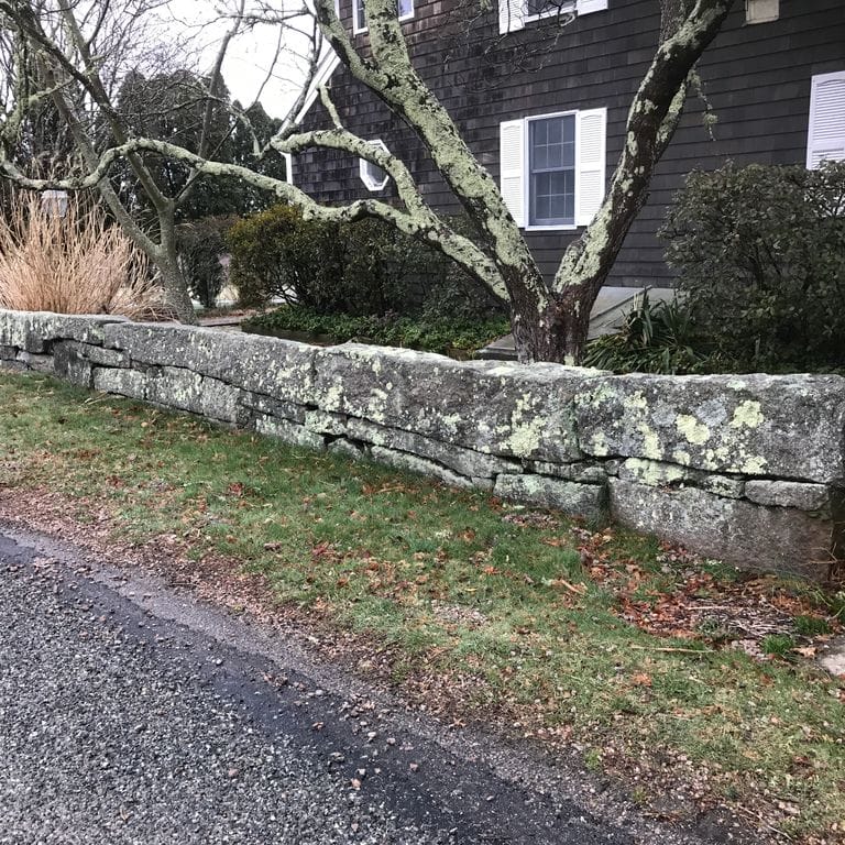 Application image for Reclaimed New England Granite Quarry Tailings - Oversized Wallstone. The image shows this product being used in a landscape wallstone application. Dominant colors shown are black and gray. The color mix creates a warm feeling.