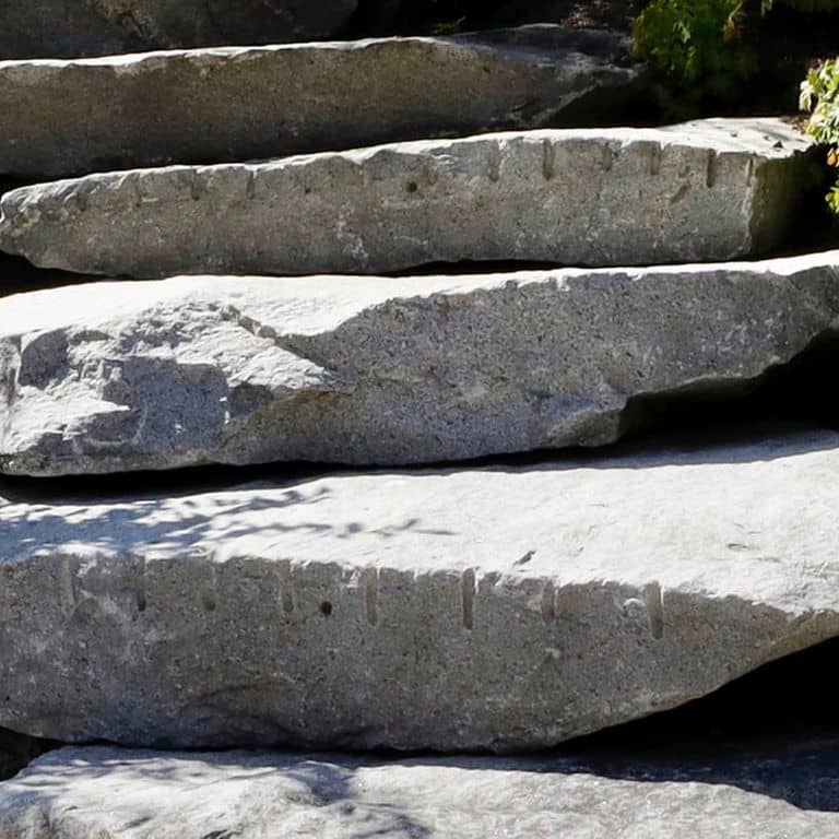 Close-up image for Reclaimed New England Granite Quarry Tailings - Steps and Landings. The surface finishes shown are split-face with rough plane and weathered. The dominant color shown is gray; with purple and white secondaries. The color mix creates a cool feeling. Regular, speckled and cloudy color patterns.