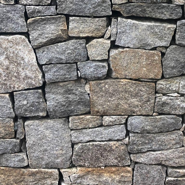 Close-up image for Reclaimed New England Granite Quarry Tailings - Wall Veneer. The surface finishes shown are split-face with rough plane and weathered. The dominant color shown is gray; with beige, black, brown, green, purple, white, tan and cream secondaries. Exhibits "movement" and the color mix creates a warm feeling. Speckled, blotched, swirled and cloudy color patterns.