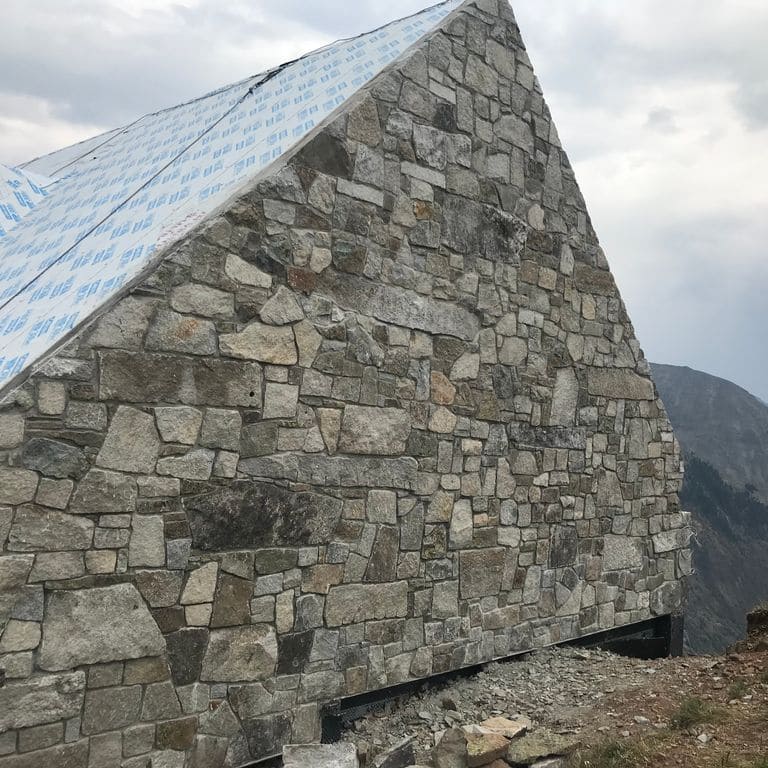 Feature image for Reclaimed New England Granite Quarry Tailings - Wall Veneer. The image shows this product being used in a full bed veneer application. The dominant color shown is gray; with beige, black, brown, green, pink, purple, white, tan and cream secondaries. Exhibits "movement". Random, speckled and blotched color patterns.