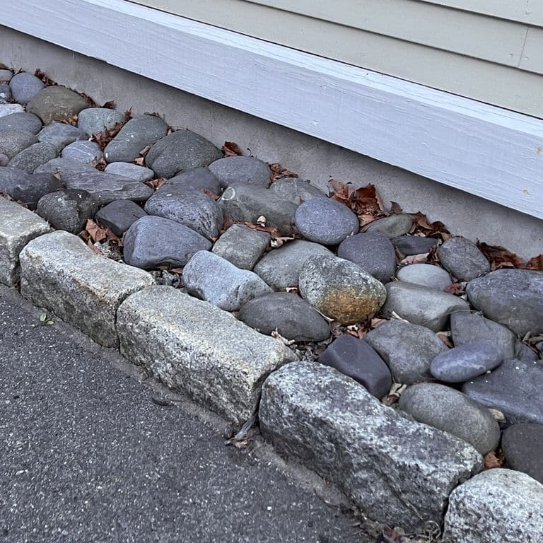 Best close-up image for Reclaimed New England Granite Cobblestones - Jumbo Edging. The image shows this product being used in a landscape curbing &amp; edging application. The surface finish shown is a combination of weathered and worn. The dominant color shown is gray; with a brown secondary. The color mix creates a cool feeling. Regular, speckled and blotched color patterns.