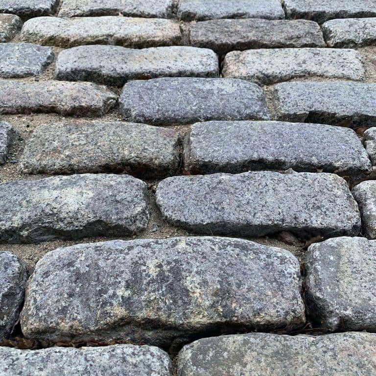 Best close-up image for Reclaimed New England Cobblestones - Jumbo Worn Top. The image shows this product being used in a driveway pavers application. The surface finish shown is a combination of weathered and worn. The dominant color shown is gray; with beige, blue, brown, green, purple, white and cream secondaries. Exhibits "movement". Speckled and blotched color patterns. Contains some mica and mineral inclusions.
