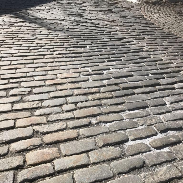 Application image for Reclaimed New England Cobblestones - Jumbo Worn Top. The image shows this product being used in a driveway pavers application. The dominant color shown is gray; with a beige secondary. The color mix creates a warm feeling. Regular, fine speckled and blotched color patterns.