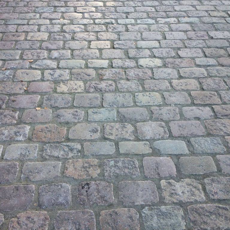 Application image for Reclaimed Swedish Granite Cobblestones - Worn Surface. The image shows this product being used in a driveway pavers application. The surface finish shown is . The dominant color shown is gray. The color mix creates a cool feeling.