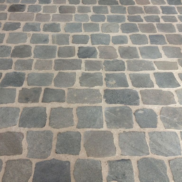 Best close-up image for Porphyry - Reclaimed European Cobblestone - Square - Flat Surface. The image shows this product being used in a patio pavers application. The surface finish shown is sawn. The dominant color shown is gray; with beige, brown, green, orange/rust, purple and tan secondaries. Regular color pattern.