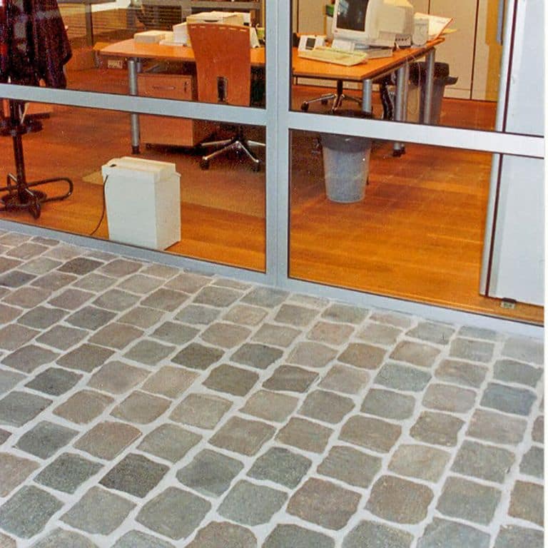 Application image for Porphyry - Reclaimed European Cobblestones - Square - Flat Surface. The image shows this product being used in a public area application. Dominant colors shown are brown and gray. The color mix creates a warm feeling.