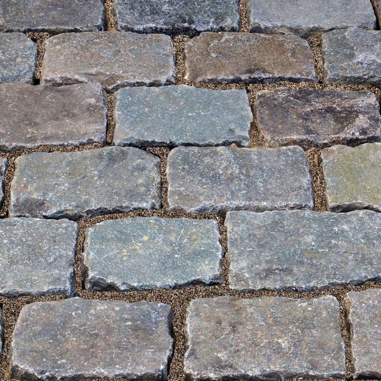 Best close-up image for Reclaimed European Porphyry Cobblestones - Rectangle - Worn. The image shows this product being used for driveway pavers, path pavers and patio pavers. The surface finish shown is . The dominant color shown is gray; with beige, black, blue, brown, green, orange/rust, purple, white and tan secondaries. Exhibits "movement" and the color mix creates a warm feeling. Regular, fine speckled, speckled and random color patterns.