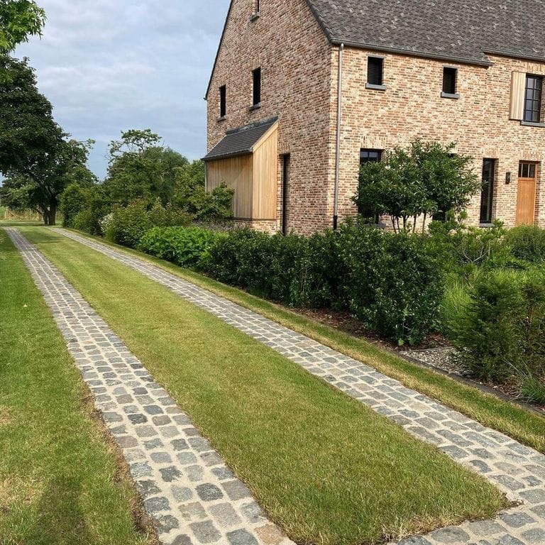 Application image for Reclaimed European Porphyry Cobblestones - Rectangle - Worn Surface. The image shows this product being used in a driveway pavers application. The surface finish shown is . Dominant colors shown are gray and tan. The color mix creates a warm feeling.