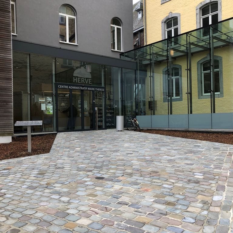 Feature image for Sandstone - Reclaimed European Cobblestones - Rectangle - Flat Surface. The image shows this product being used for patio pavers and public area. The surface finish shown is sawn. Dominant colors shown are brown, gray and tan; with beige and cream secondaries. Fine speckled color pattern.