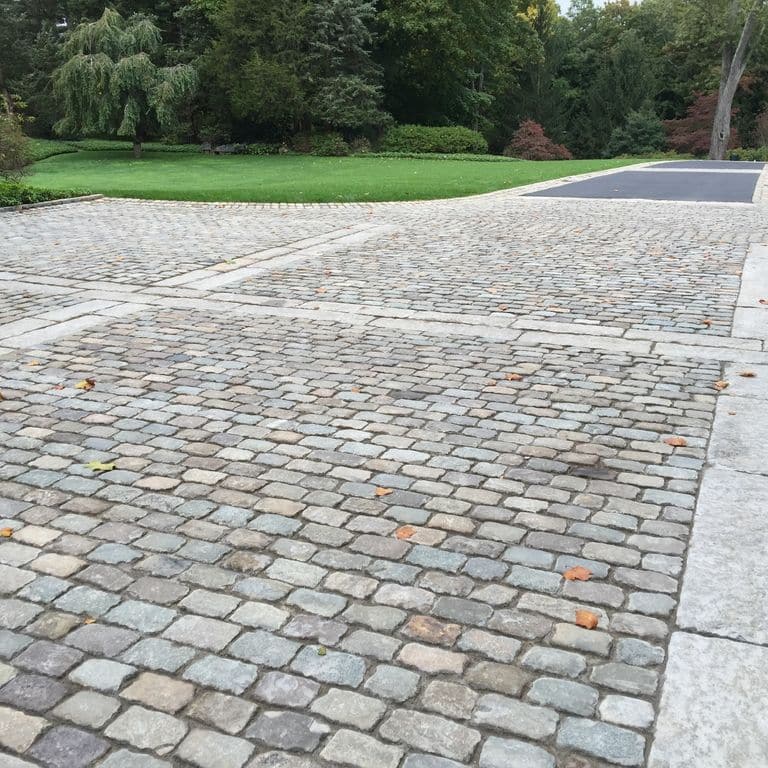 Application image for Reclaimed European Sandstone Cobblestones - Rectangle - Worn Surface. The image shows this product being used in a driveway pavers application. The surface finish shown is . The dominant color shown is gray. The color mix creates a warm feeling.