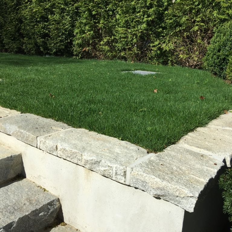 Application image for Reclaimed Granite Capstones. The image shows this product being used in a wallstone cap application. This is a landscape stone for outdoor commercial and residential applications. Suitable for general use, freeze-thaw conditions and low heat absorption surfaces situations. Moderate to higher on the price spectrum.