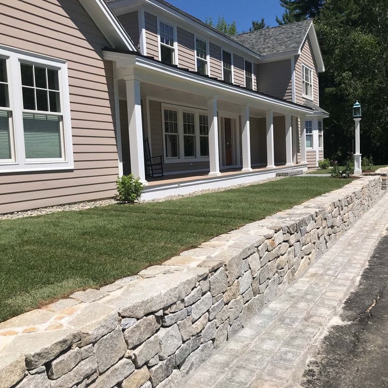 Application image for Granite - Reclaimed New England Quarry Tailings - Wallstone. The image shows this product being used in a landscape wallstone application. The dominant color shown is gray.