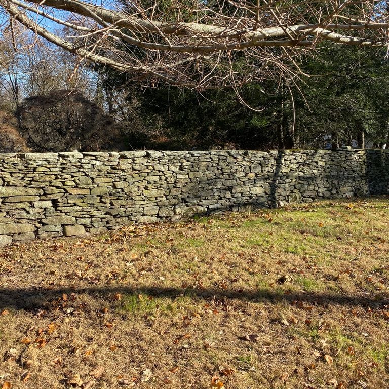 Application image for New England Fieldstone Flats - Wallstone. The image shows this product being used in a landscape wallstone application. The surface finish shown is weathered. Dominant colors shown are brown and gray. The color mix creates a warm feeling.