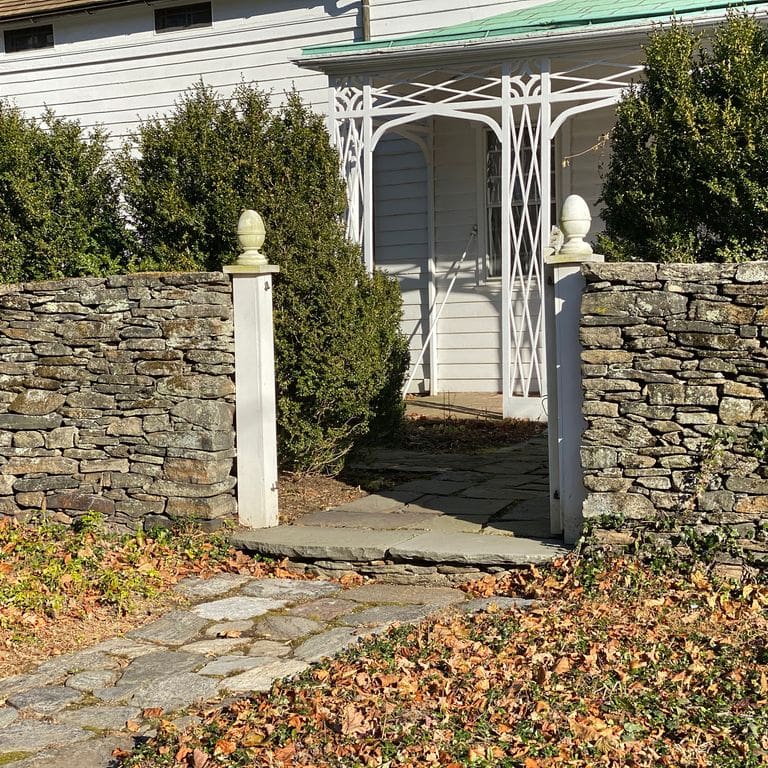Application image for New England Fieldstone Flats - Wallstone. The image shows this product being used in a landscape wallstone application. The surface finish shown is weathered. Dominant colors shown are brown, gray and tan; with beige, green, orange/rust, white and cream secondaries. Exhibits "movement" and the color mix creates a warm feeling. Fine speckled, blotched and cloudy color patterns.