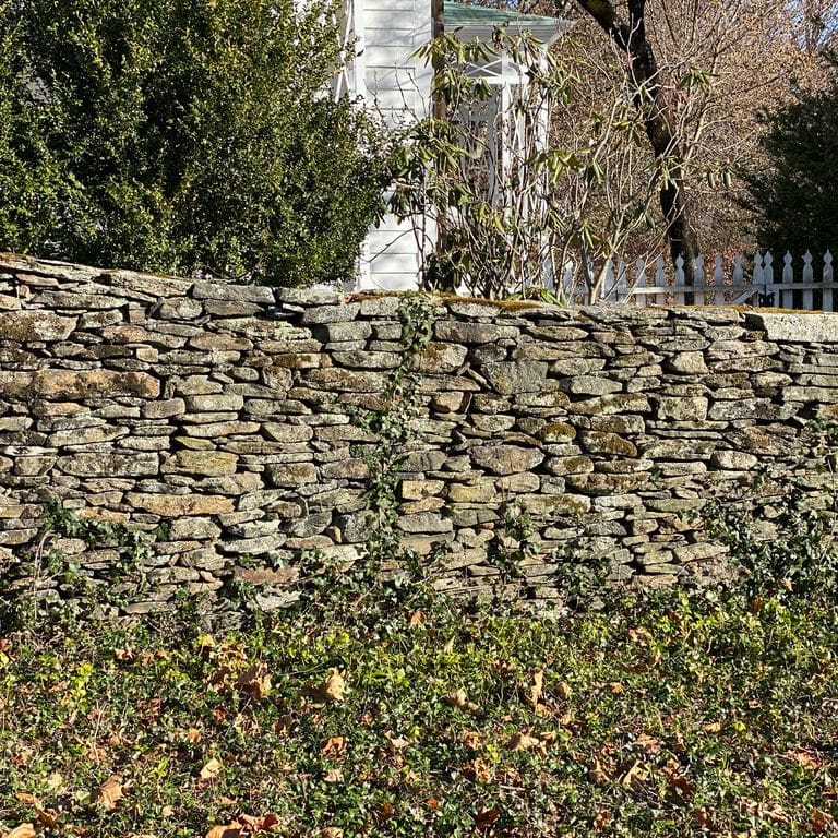 Application image for New England Fieldstone Flats - Wallstone. The image shows this product being used in a landscape wallstone application. The surface finish shown is weathered. The dominant color shown is gray. The color mix creates a warm feeling.