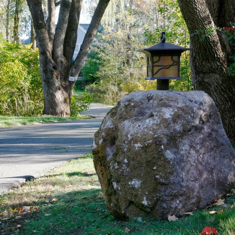 Feature image for New England Fieldstone Boulders &amp; Ledgestone - Fountains &amp; Lights. The image shows this product being used in a garden accents application. The surface finish shown is weathered. The dominant color shown is gray; with black, blue, brown and purple secondaries. Blotched, random and cloudy color patterns.