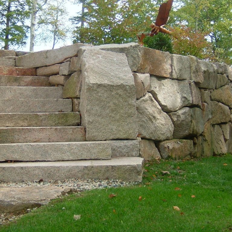 Feature image for Reclaimed Granite Step - Live Edge. The image shows this product being used in a monolithic steps application. The dominant color shown is gray; with beige, brown, green, orange/rust, white and tan secondaries. Fine speckled and blotched color patterns.