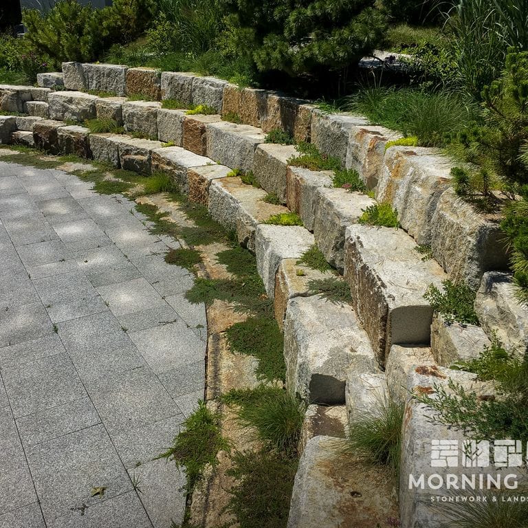 Application image for Reclaimed Granite Bridge Blocks - Benches and Seating. The image shows this product being used in a seating &amp; benches application. This is a landscape stone for outdoor commercial and residential applications. Suitable for general use, freeze-thaw conditions, low heat absorption surfaces and low slipperiness surfaces situations. Relatively higher in price.