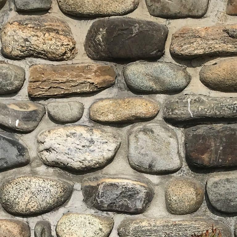 Close-up image for Beach Rounds Veneer. The surface finishes shown are natural and worn. Dominant colors shown are beige, brown, gray and tan; with black, green, orange/rust, white and cream secondaries. Exhibits "movement" and the color mix creates a warm feeling. Random, speckled, blotched and swirled color patterns.
