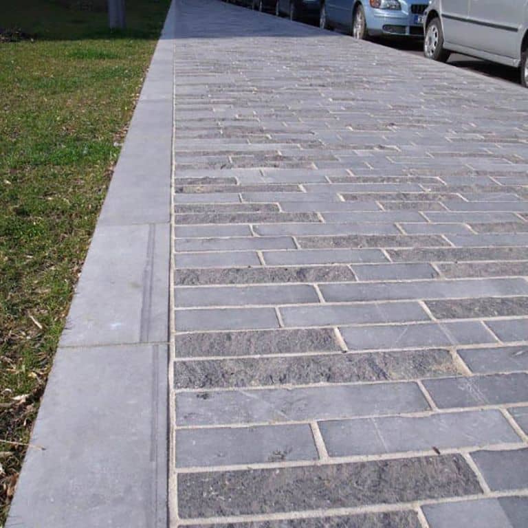 Feature image for Limestone - Belgian Bluestone - Pavers. The image shows this product being used in a path pavers application. Dominant colors shown are blue and gray; with a white secondary. The color mix creates a cool feeling. Solid, speckled and cloudy color patterns.