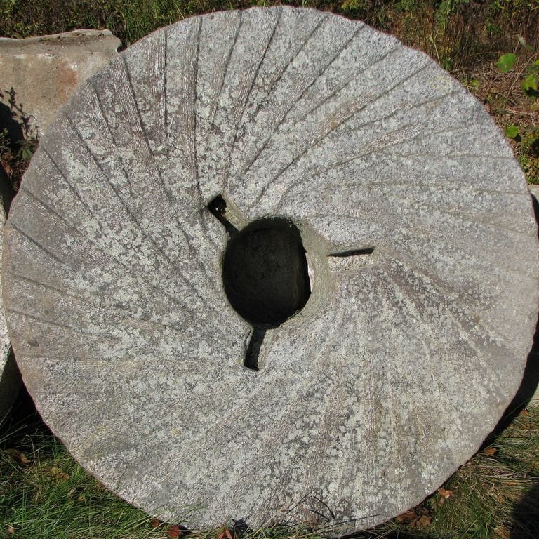 Close-up image for Reclaimed Granite - Millstone. The surface finishes shown are weathered and worn. The dominant color shown is gray; with beige, green, orange/rust, purple, white and tan secondaries. Exhibits "movement". Speckled, fine speckled and blotched color patterns.