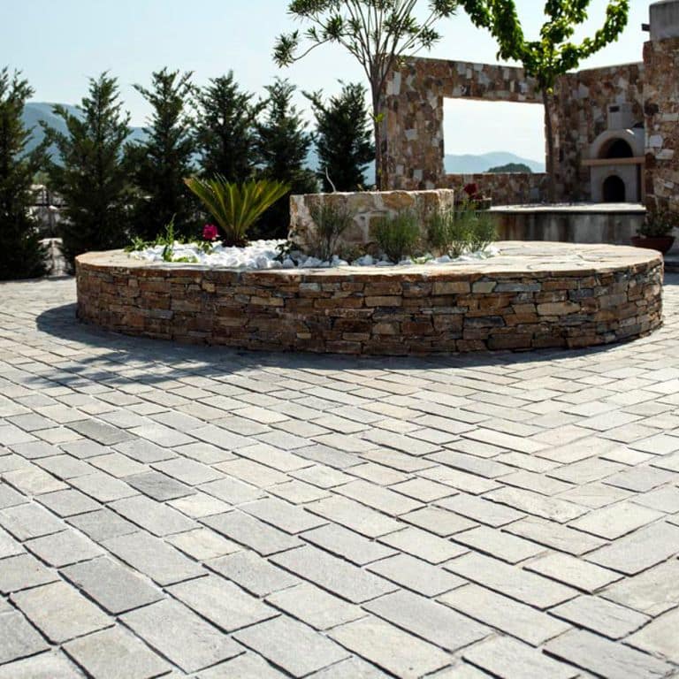Feature image for Greek Quartzite Slate - Grey - Cobblestones. The image shows this product being used for driveway pavers and patio pavers. The dominant color shown is gray; with beige, brown, white and cream secondaries. The color mix creates a cool feeling. Speckled color pattern.