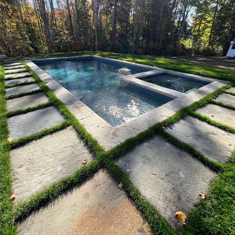 Application image for Full Color Bluestone - Natural Cleft Pavers. The image shows this product being used in a pool deck pavers application. The surface finish shown is natural cleft. Dominant colors shown are blue, gray and tan; with brown, orange/rust and tan secondaries. Exhibits "movement".