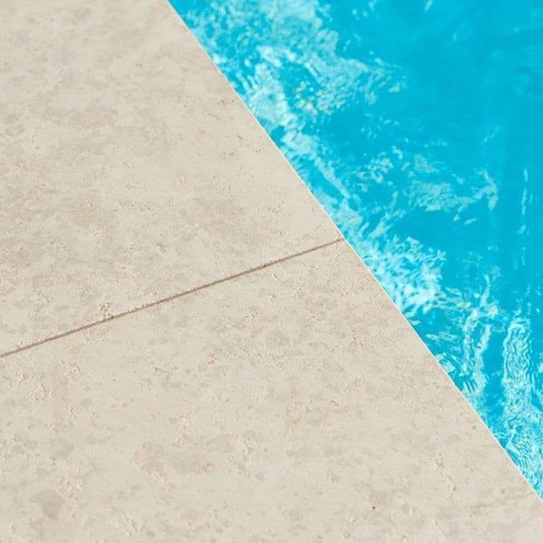 Best close-up image for Limestone- Mountain Hard Beige - Pool Coping. The image shows this product being used for pool coping and pool deck pavers. The surface finish shown is sand blasted. Dominant colors shown are beige and cream; with gray, white and tan secondaries. Exhibits "movement". Solid, regular, marbled, blotched and cloudy color patterns.