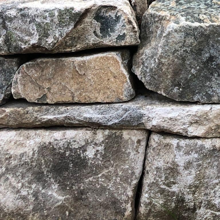Close-up image for Black Mountain Granite Natural - Wallstone. The surface finishes shown are split-face and split-face with rough plane. The dominant color shown is gray; with beige, black, brown, green, orange/rust, purple, white and tan secondaries. Exhibits "movement". Random, speckled and blotched color patterns. Contains lots of mica.