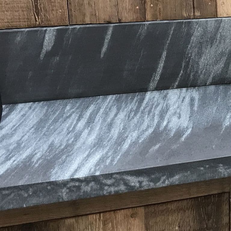 Close-up image for Mystic Mountain Countertops. The surface finish shown is honed. Dominant colors shown are black, blue and gray; with green and white secondaries. Exhibits "movement" and the color mix creates a cool feeling. Linear and streaked color patterns.