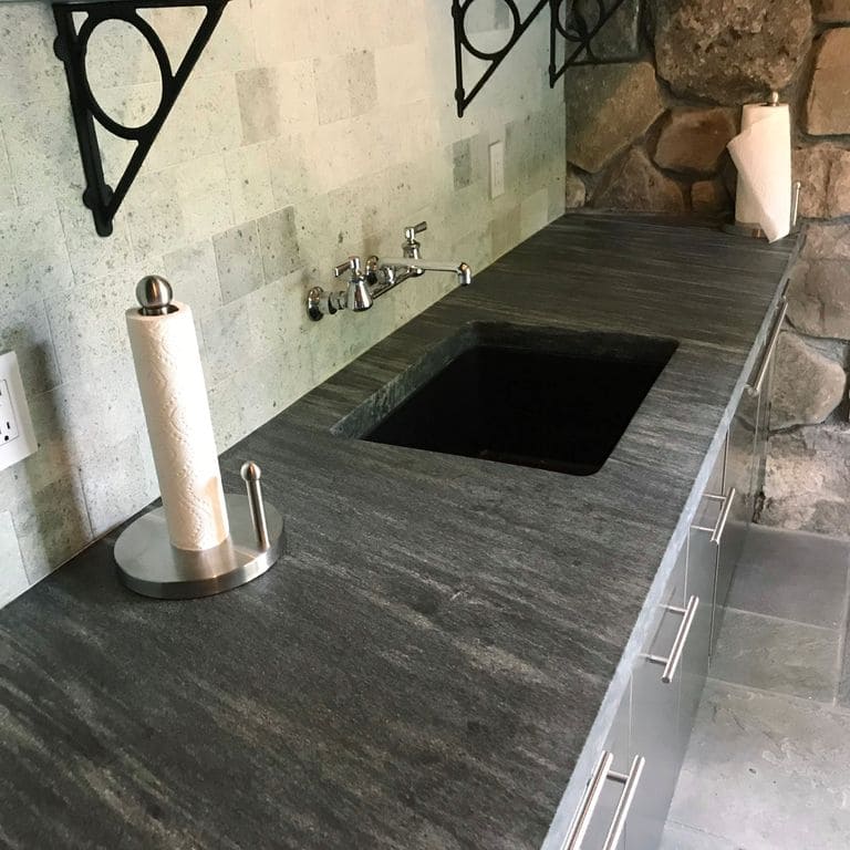 Feature image for Mystic Mountain Countertops. The image shows this product being used in a countertop slabs application. The dominant color shown is gray; with black, brown, green and tan secondaries. Exhibits "movement" and the color mix creates a cool feeling. Linear color pattern.