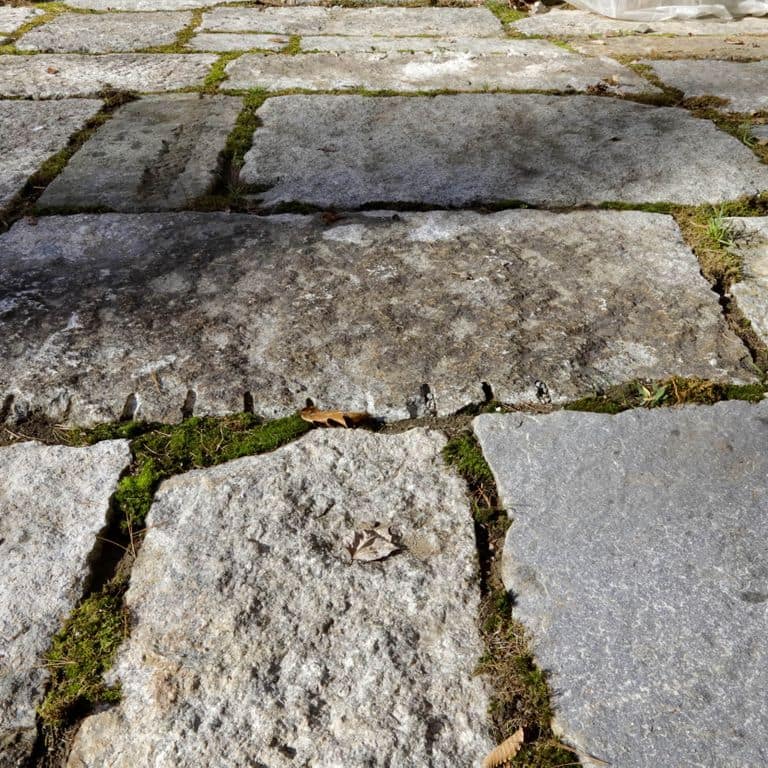 Best close-up image for Reclaimed Granite Block - Quarry Skin Pavers. The image shows this product being used in a patio pavers application. The surface finish shown is a combination of split-face with flat plane, split-face with rough plane and weathered. The dominant color shown is gray; with brown, pink, purple, white and cream secondaries. Exhibits "movement" and the color mix creates a cool feeling. Fine speckled, speckled, blotched, random and cloudy color patterns.
