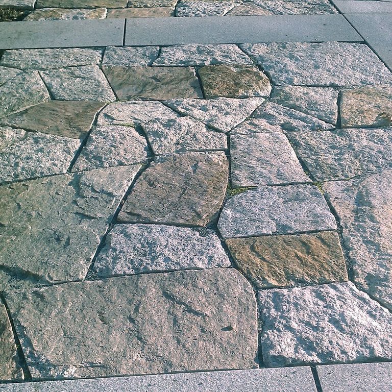 Application image for Reclaimed Granite Block - Quarry Skin Pavers. The image shows this product being used in a patio pavers application. The surface finish shown is a combination of split-face with flat plane, split-face with rough plane and weathered. The dominant color shown is gray; with orange/rust and tan secondaries. The color mix creates a cool feeling.