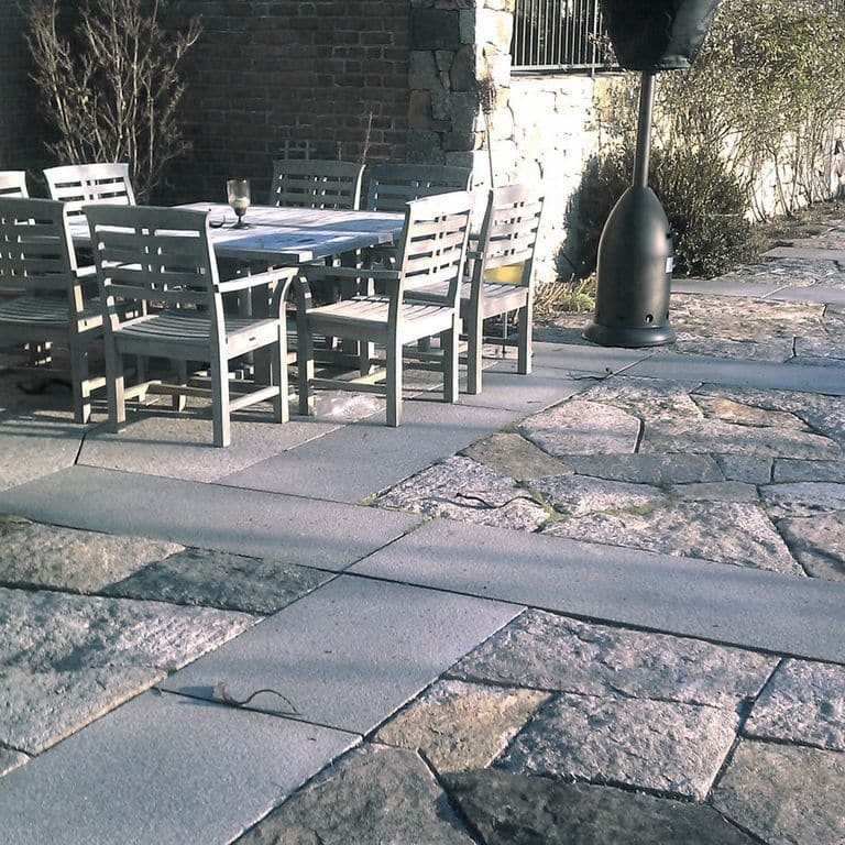 Application image for Reclaimed Granite Block - Quarry Skin Pavers. The image shows this product being used in a patio pavers application. The surface finish shown is . The dominant color shown is gray. The color mix creates a cool feeling. Blotched color pattern.
