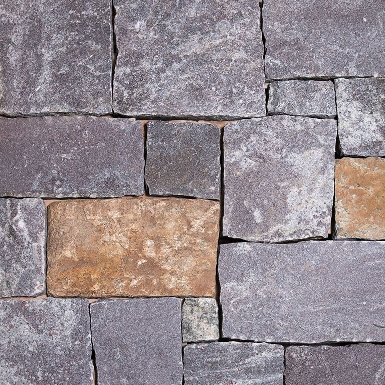 Feature image for Dolph Pond Granite - Veneer. The image shows this product being used in a full bed veneer application. The dominant color shown is gray; with beige, brown, orange/rust, purple, white and tan secondaries. Exhibits "movement". Blotched and cloudy color patterns.