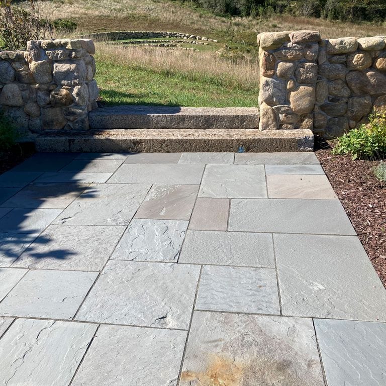 Application image for Bluestone Natural Cleft Blue/Gray - Dimensional Cut Pavers. The image shows this product being used in a patio pavers application. The surface finish shown is natural cleft. Dominant colors shown are gray and white. The color mix creates a cool feeling.