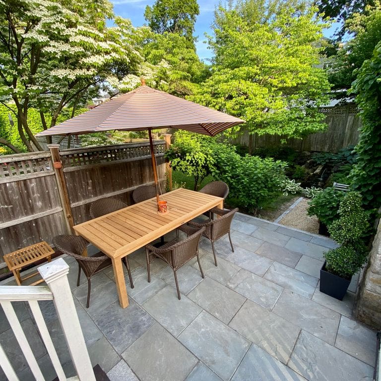 Feature image for Clear Color Mix Bluestone - Natural Cleft Dimensional Cut Pavers. The image shows this product being used in a patio pavers application. The surface finish shown is natural cleft. Dominant colors shown are blue, green and gray. The color mix creates a cool feeling.