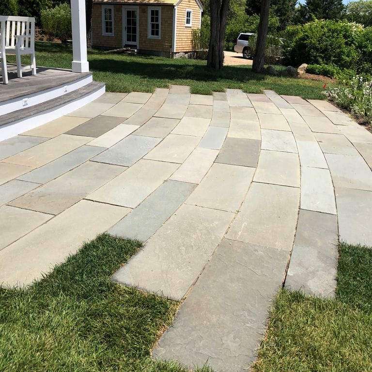 Application image for Clear Color Mix Bluestone - Natural Cleft Dimensional Cut Pavers. The image shows this product being used in a patio pavers application. Dominant colors shown are beige, gray and cream; with white and tan secondaries. Exhibits "movement" and the color mix creates a warm feeling. Solid and cloudy color patterns.