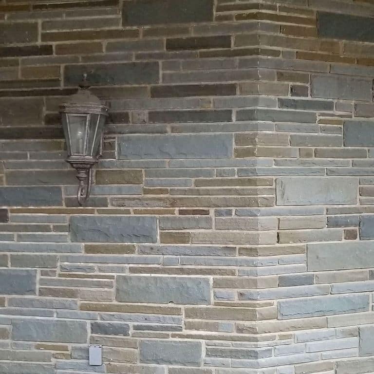 Application image for Full Color Bluestone - Natural Cleft Full Bed Veneer. The image shows this product being used in a full bed veneer application. The surface finish shown is split-face with rough plane. Dominant colors shown are gray and tan; with beige, blue, brown, green, purple and white secondaries. Exhibits "movement". Random color pattern.
