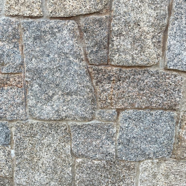 Best close-up image for Granite - Cape Neddick Clear - Full Bed Veneer. The image shows this product being used in a full bed veneer application. The surface finish shown is split-face with flat plane. The dominant color shown is gray; with brown, white and cream secondaries. Speckled color pattern.