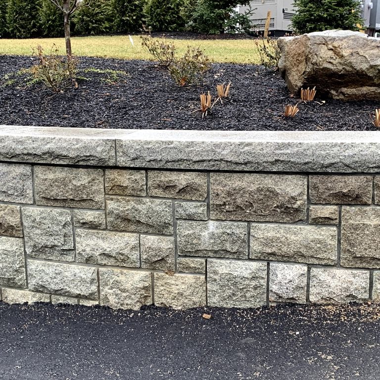 Application image for Cape Neddick Granite Clear - Full Bed Veneer. The image shows this product being used for wallstone cap and full bed veneer. The surface finish shown is rockfaced. The dominant color shown is gray. The color mix creates a warm feeling. Regular color pattern.