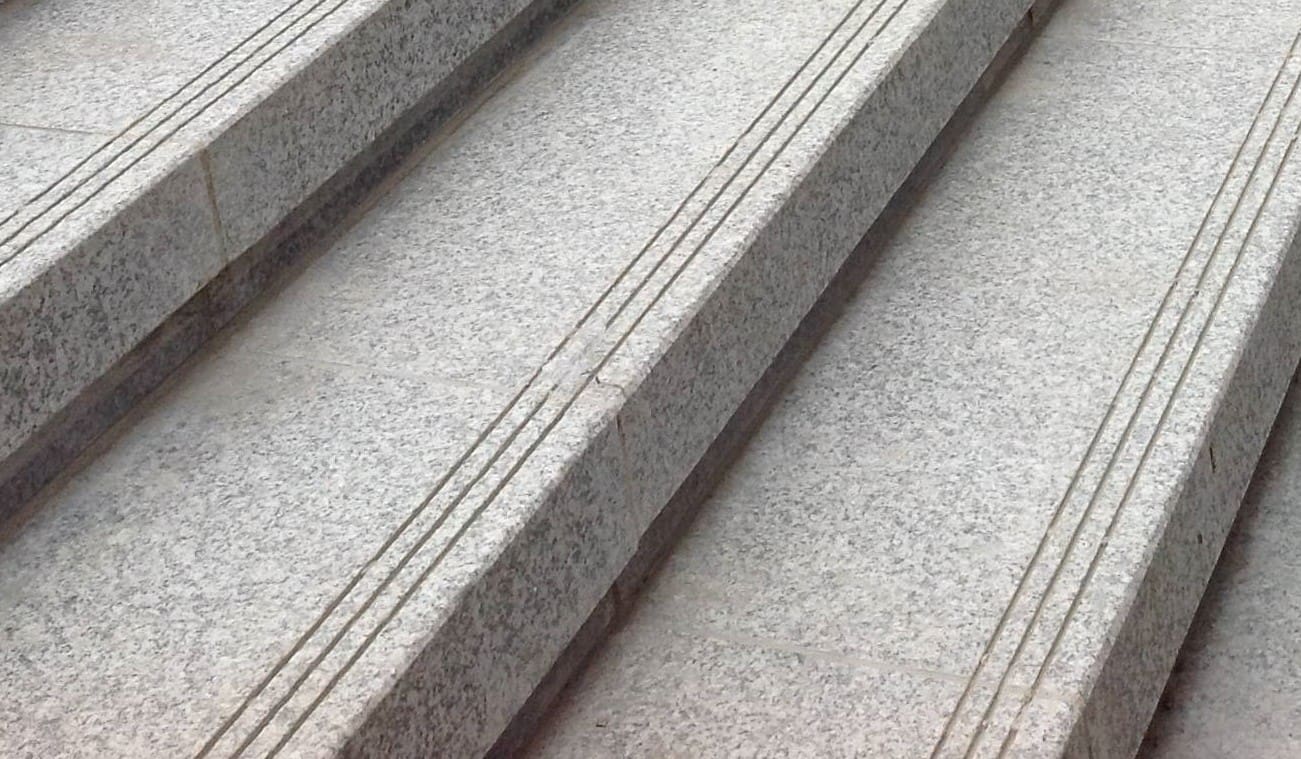 Close-up image for Gray Ariz Granite - Treads. The surface finish shown is sand blasted. The dominant color shown is gray; with beige, purple and white secondaries. The color mix creates a cool feeling. Speckled and coarse speckled color patterns. Contains some mica and mineral inclusions.