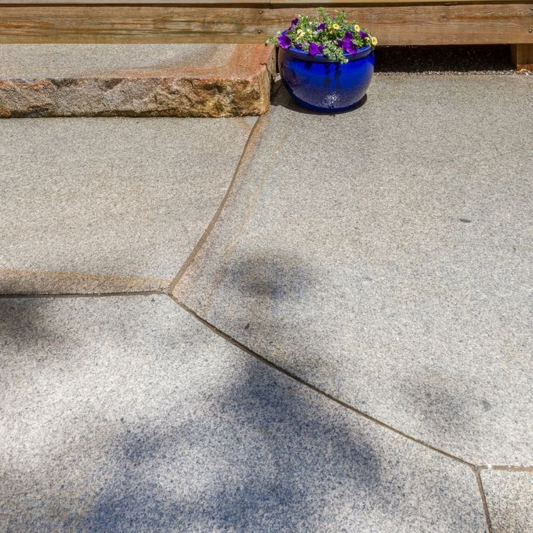 Feature image for Cape Neddick Granite Full Color - Cut to Fit Pavers. The image shows this product being used in a patio pavers application. The design pattern shown is irregular flagging sawn flat edges &amp; irregular sawn edges. The dominant color shown is gray; with beige, brown, pink and white secondaries. Fine speckled color pattern.