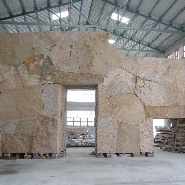 Feature image for Quarried Chinese Granite - Quarry Skin Veneer. The image shows this product being used for full bed veneer and interior cladding. The surface finish shown is split-face with flat plane. Dominant colors shown are beige, brown, gray and tan; with an orange/rust secondary. Exhibits "movement" and the color mix creates a warm feeling. Random color pattern.